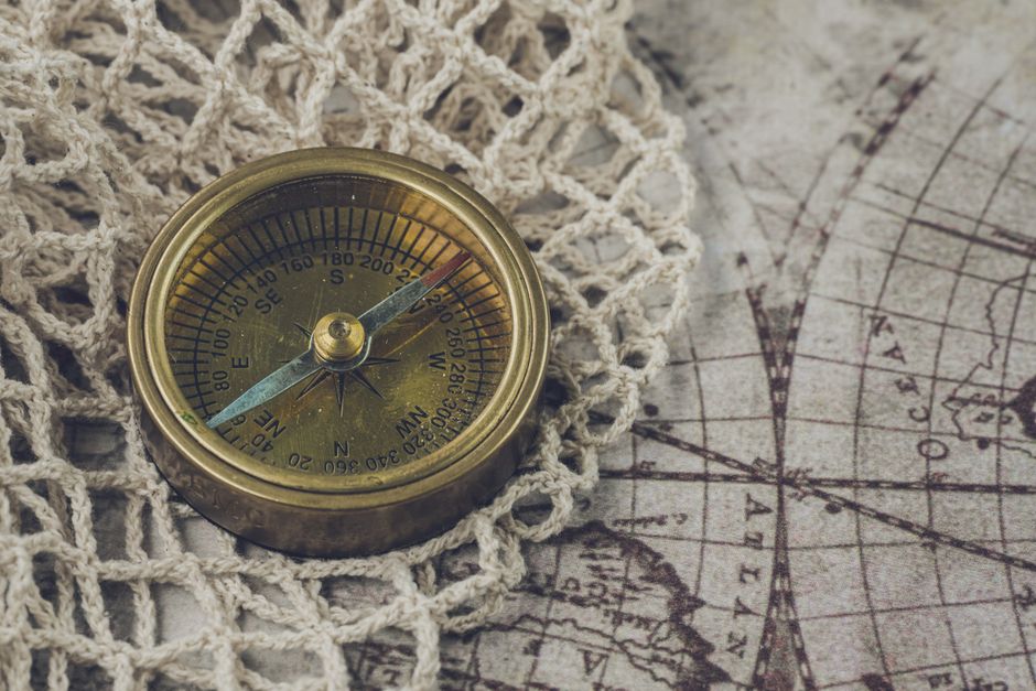 Brass compass resting on an antique world map with crochet details, symbolizing navigation and exploration.