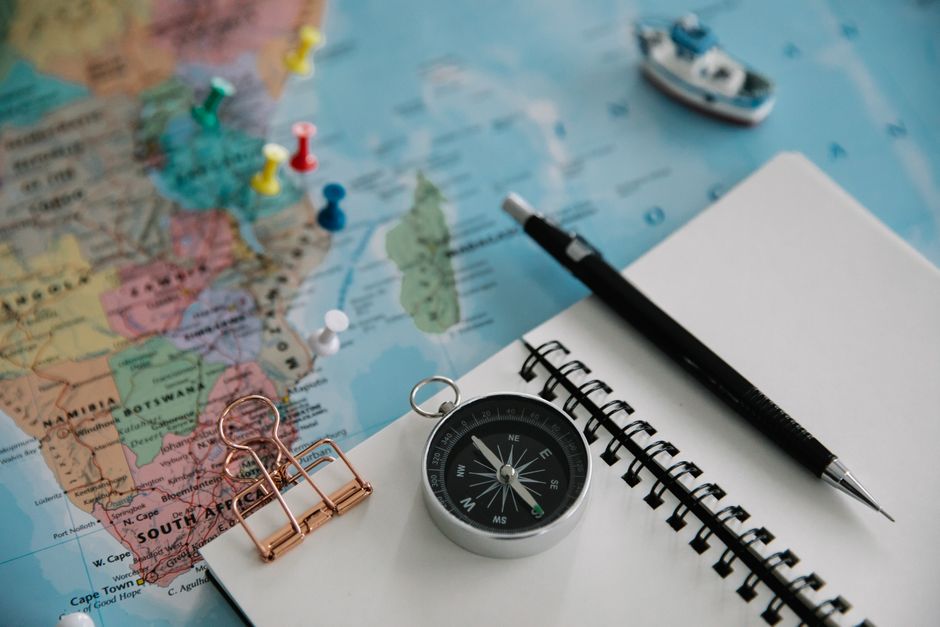 Flat lay of travel planning tools including a map, compass, notebook, and pen.